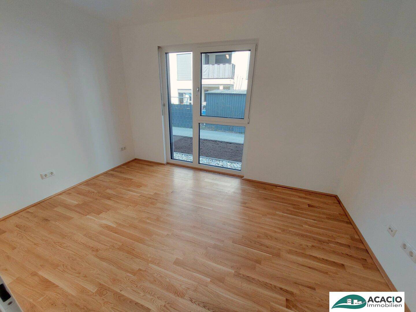 Helles Zimmer mit Holzboden und großen Fenstern, die viel Tageslicht hereinlassen.