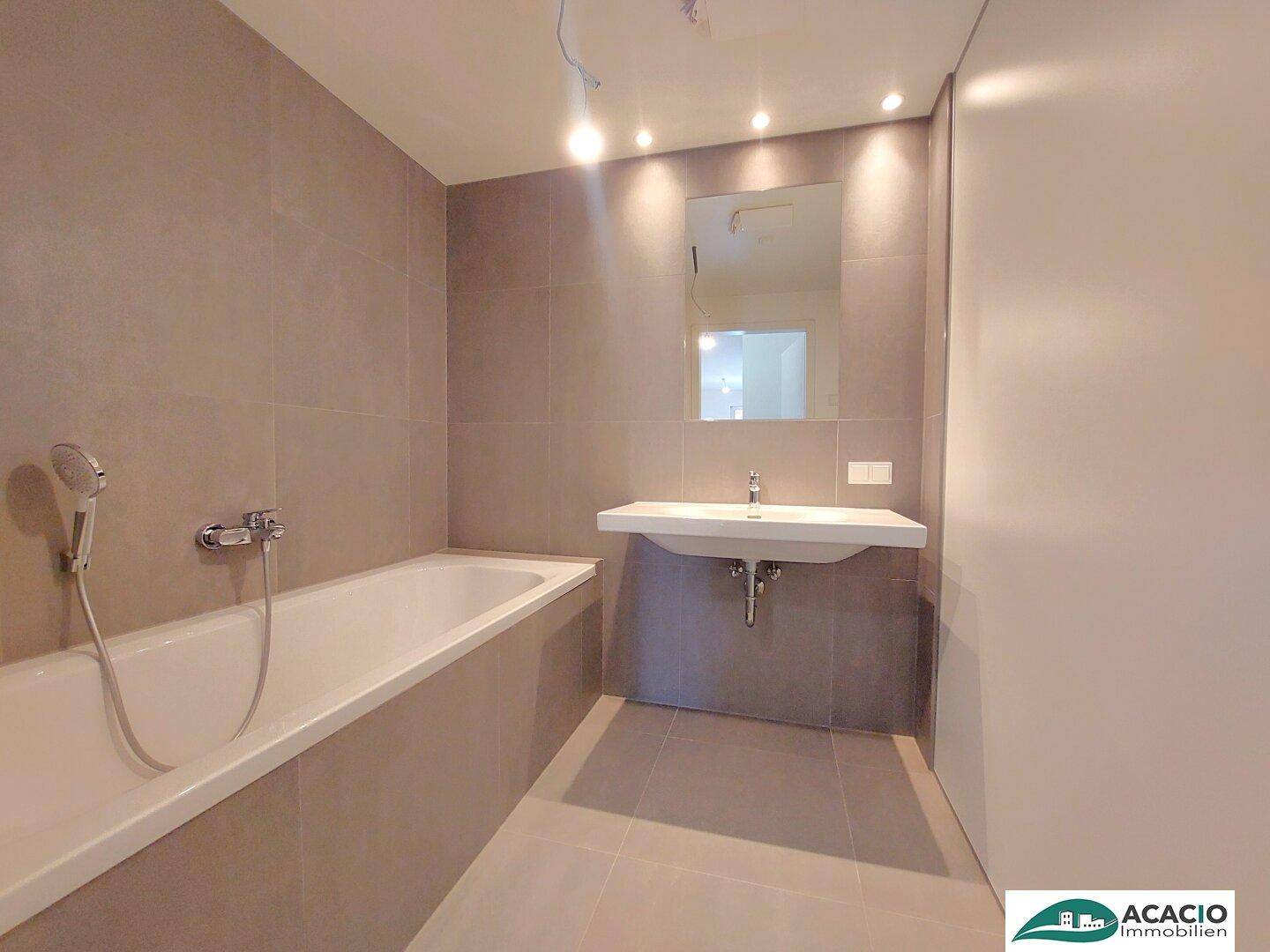 Modernes Badezimmer mit Badewanne, Waschbecken und grauen Fliesen, in neuwertigem Zustand.