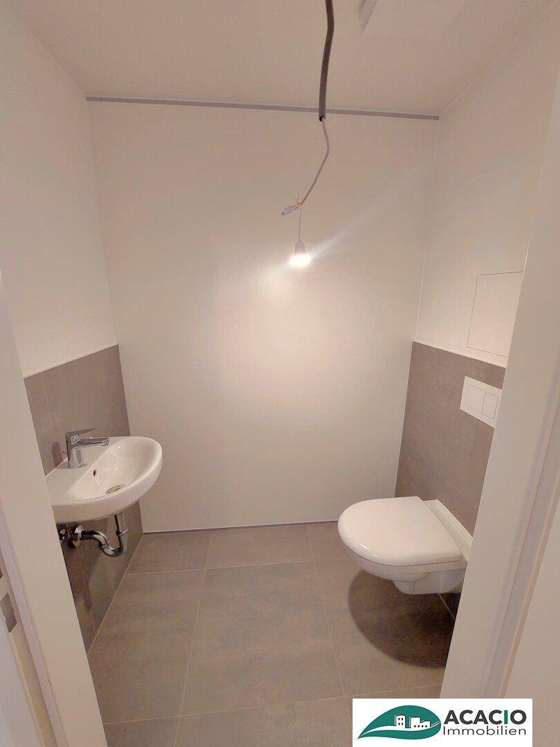 Separates Gäste-WC mit wandhängender Toilette, kleinem Waschbecken und grauen Fliesen.