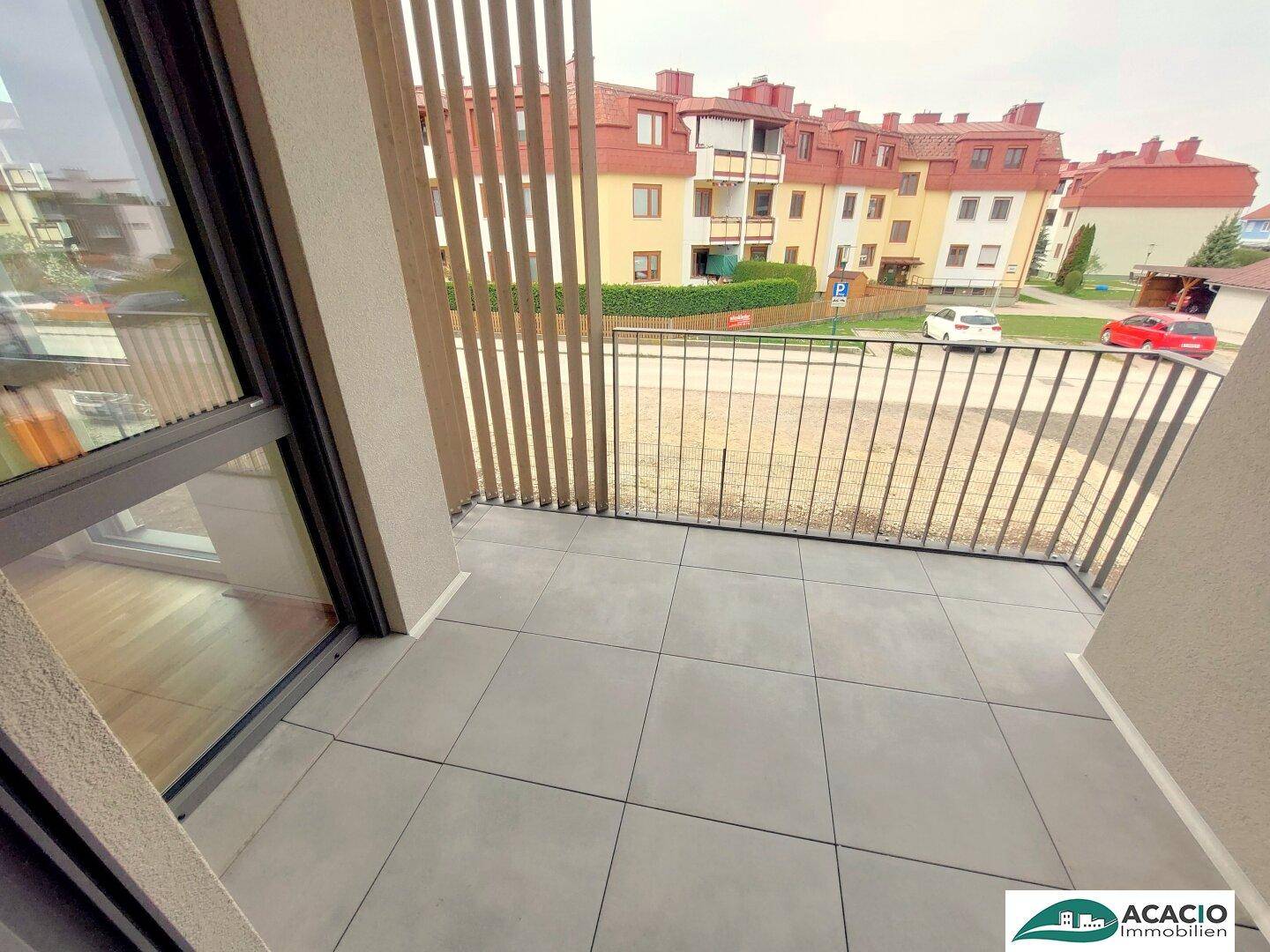 Balkon mit Fliesenboden und Blick auf die umliegenden Gebäude und eine grüne Fläche.