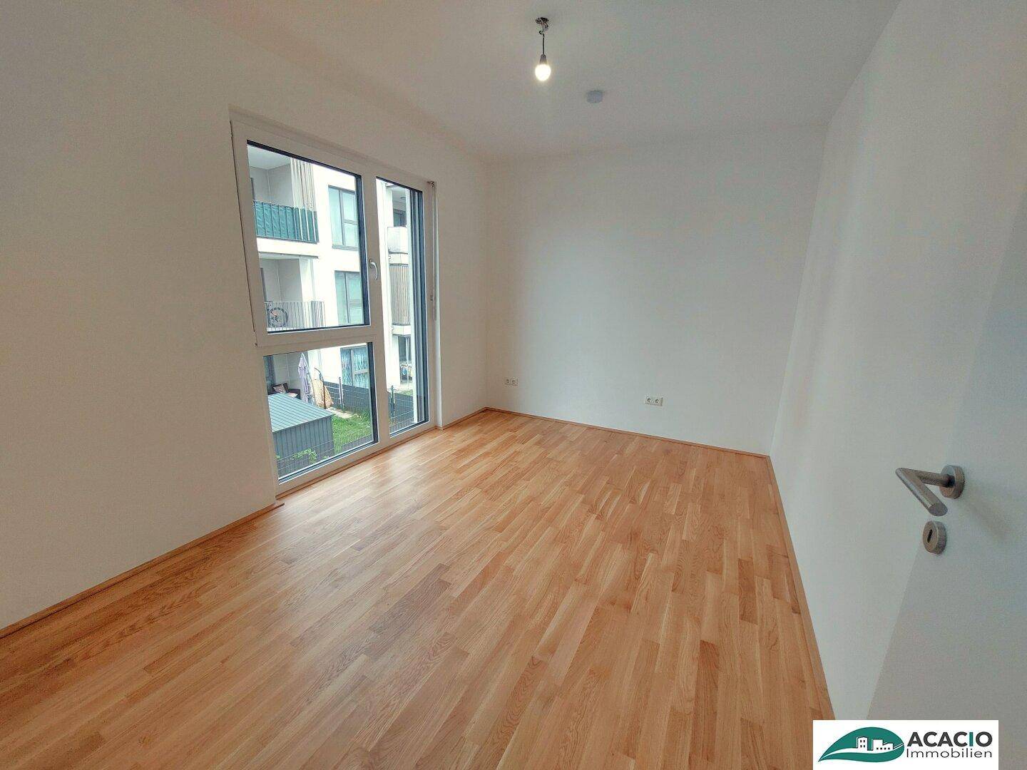 Helles Schlafzimmer mit Parkettboden und großem Fenster, das viel Tageslicht hereinlässt.