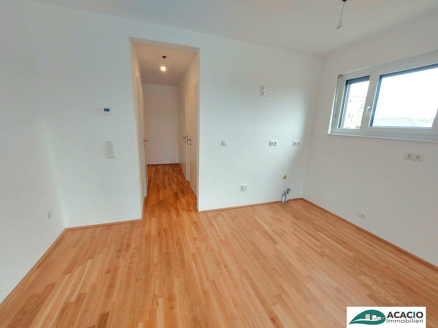 Geräumiges, leeres Zimmer mit Parkettboden und Zugang zu einem Flur, bereit zum Einzug.