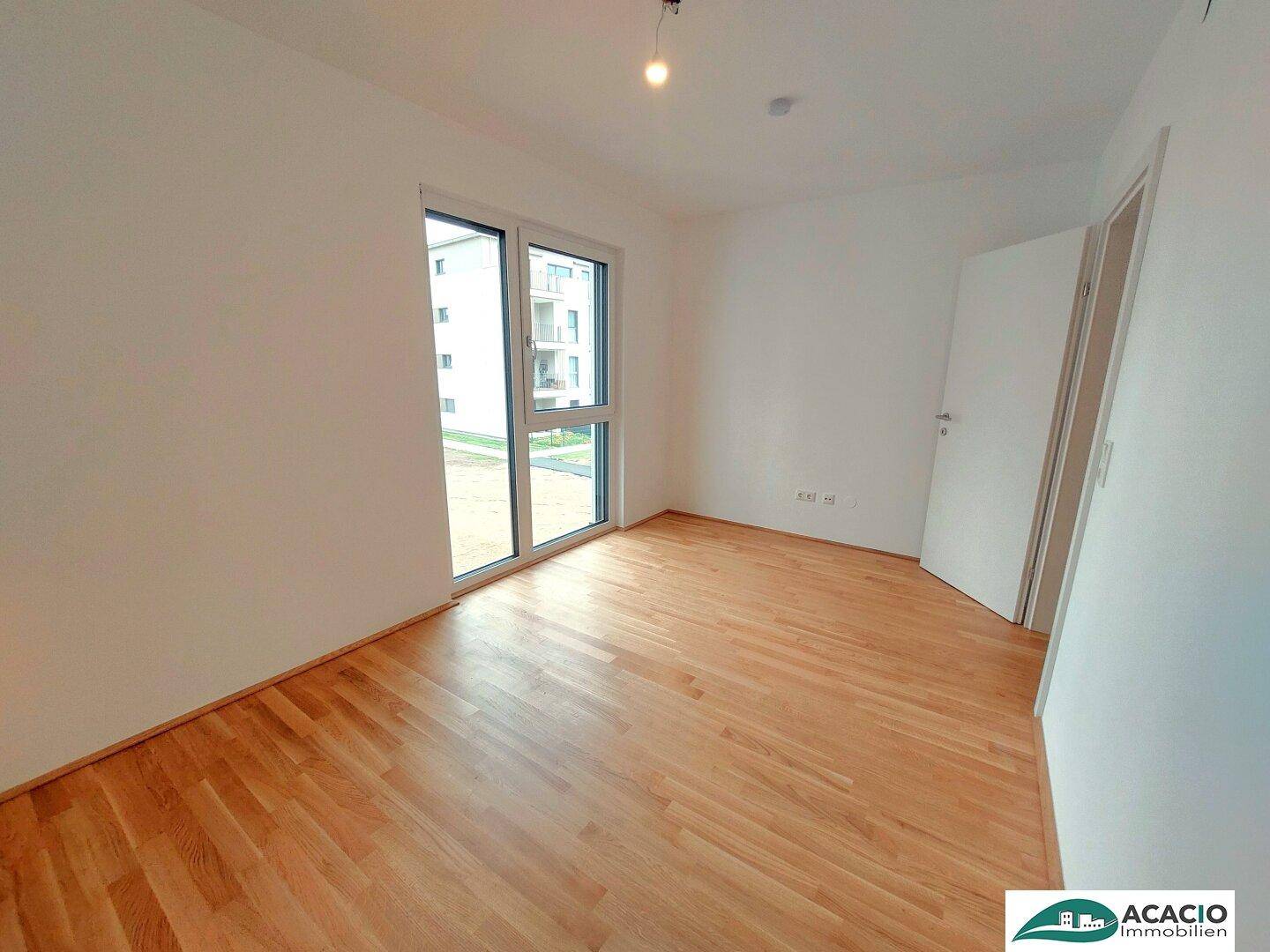 Leeres Zimmer mit Parkettboden und großen Fenstern, die viel Tageslicht hereinlassen.