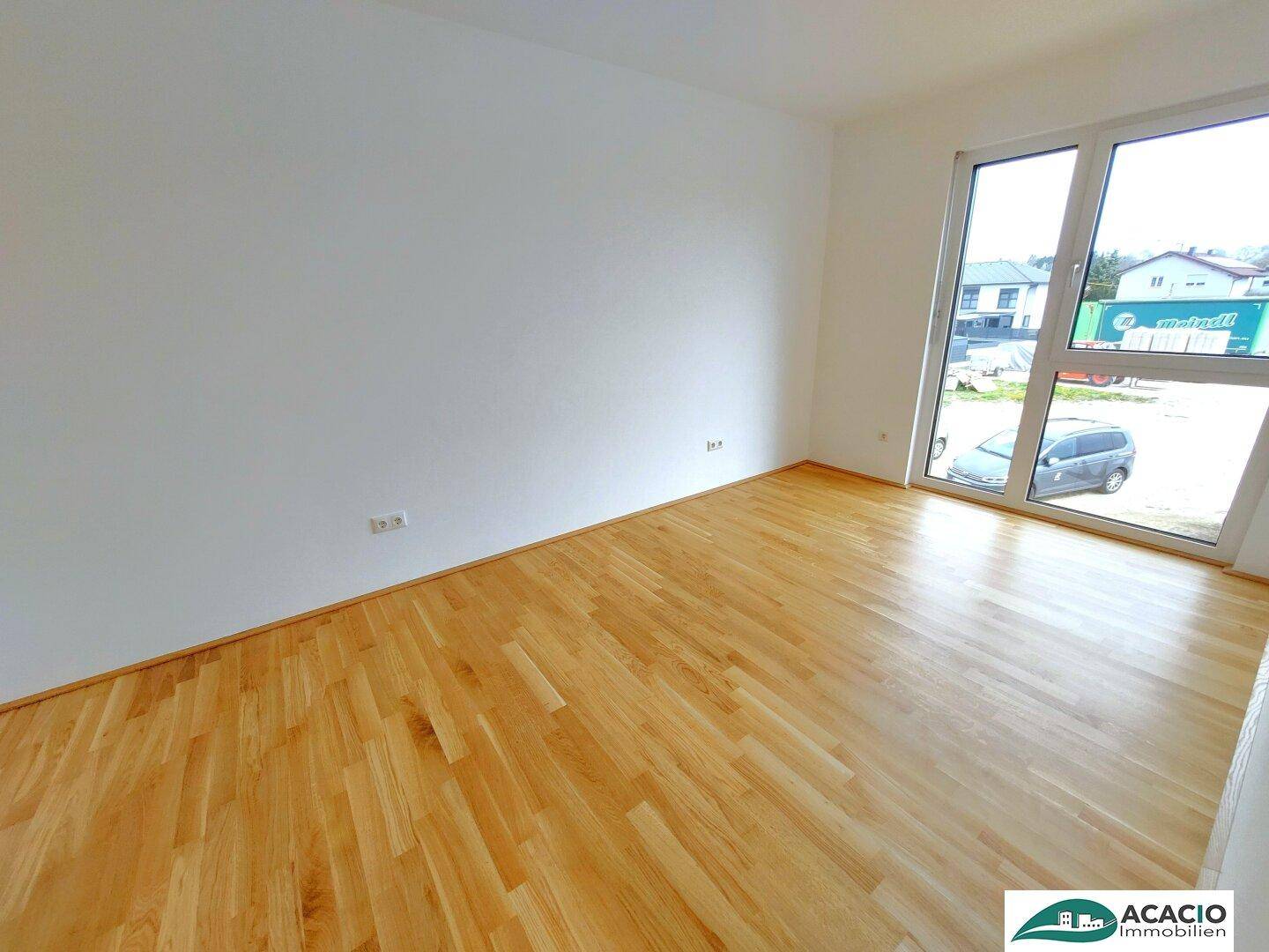 Heller Raum mit Parkettboden und großem Fenster, das einen Blick auf die Straße bietet.