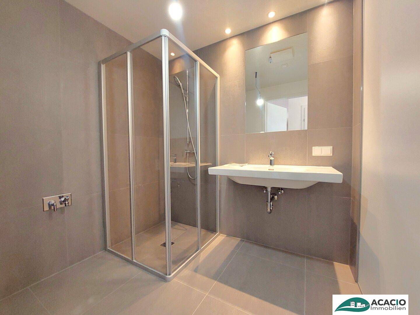 Modernes Badezimmer mit Duschkabine, großem Waschbecken und grauen Wand- und Bodenfliesen.