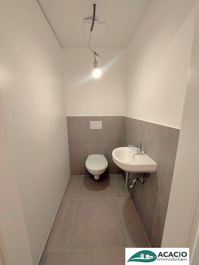 Modernes Gäste-WC mit Wand-WC, kleinem Waschbecken und grauen Fliesen.