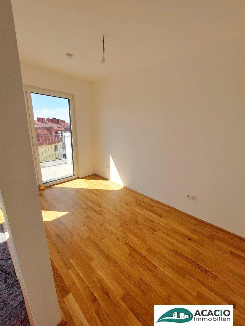 Helles Zimmer mit Holzboden und Zugang zu einem Balkon, ideal als Schlafzimmer oder Wohnbereich.