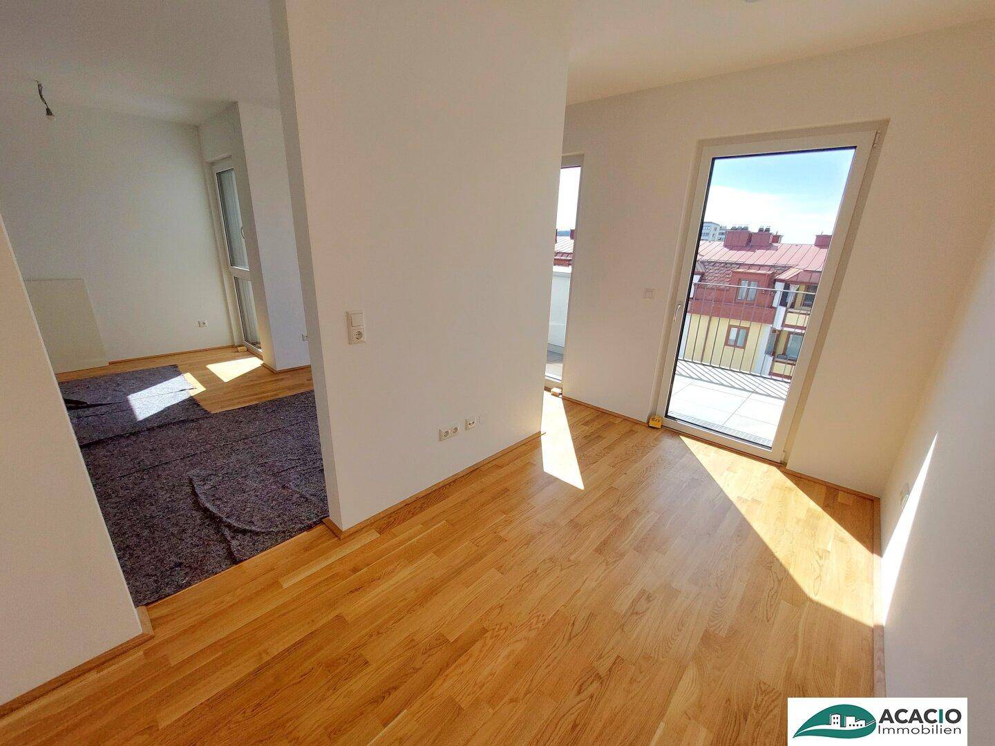 Heller Wohnbereich mit Holzboden und Zugang zu einem weiteren Zimmer sowie einem Außenbereich.