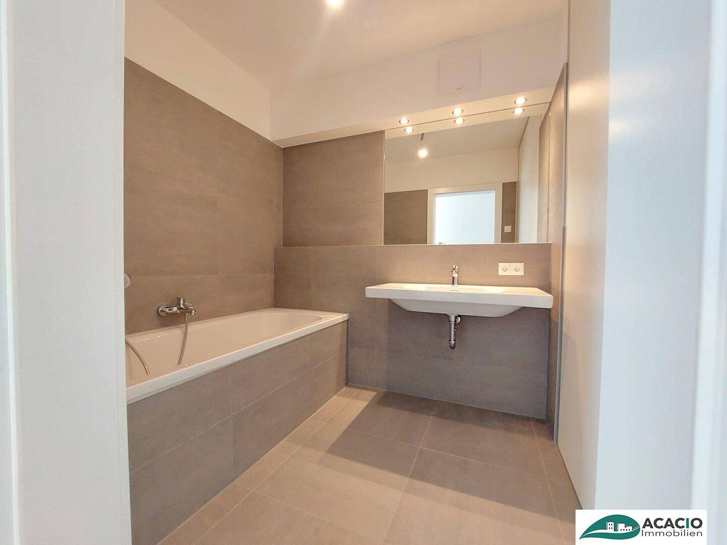 Modernes Badezimmer mit Badewanne, Waschtisch und großem Spiegel, ausgestattet mit grauen Fliesen.