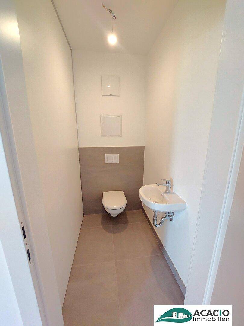 Kleines Gäste-WC mit wandhängender Toilette und Handwaschbecken, modern gefliest.