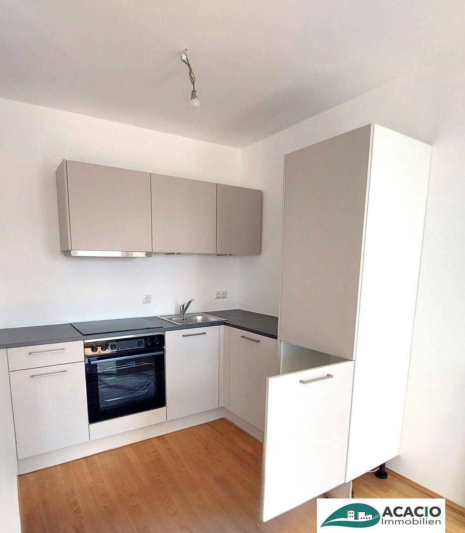 Moderne Einbauküche mit weißen Schränken, dunkler Arbeitsplatte und integriertem Backofen in neuwertigem Zustand.