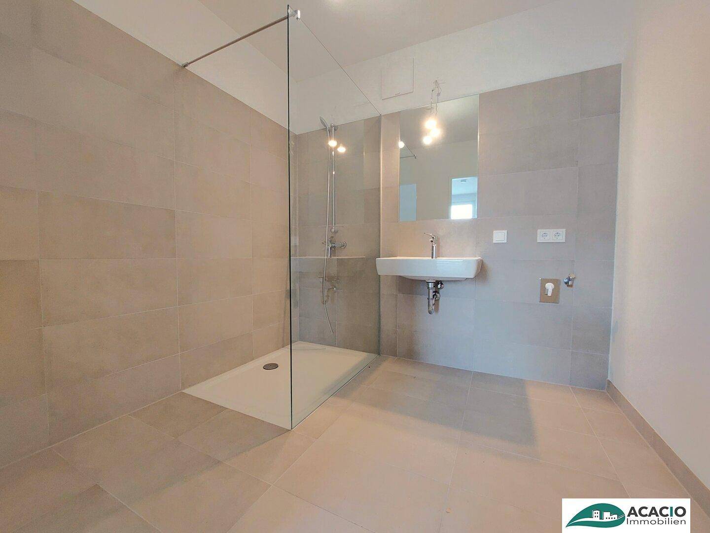 Modernes Badezimmer mit großformatigen grauen Fliesen, ebenerdiger Dusche und elegantem Waschbecken.