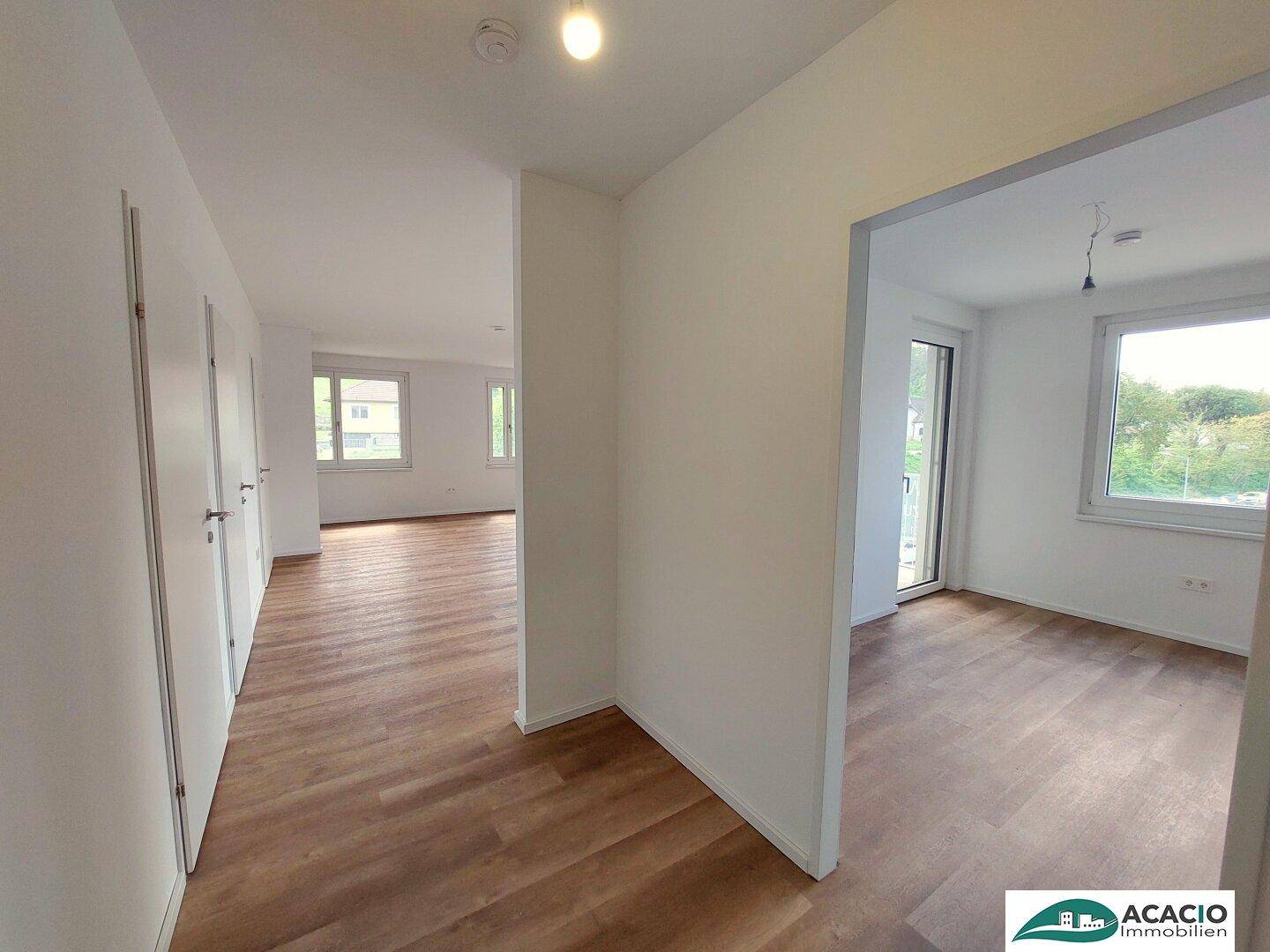 Heller Flur mit Holzboden und weißen Wänden, der zu verschiedenen Zimmern der Wohnung führt.