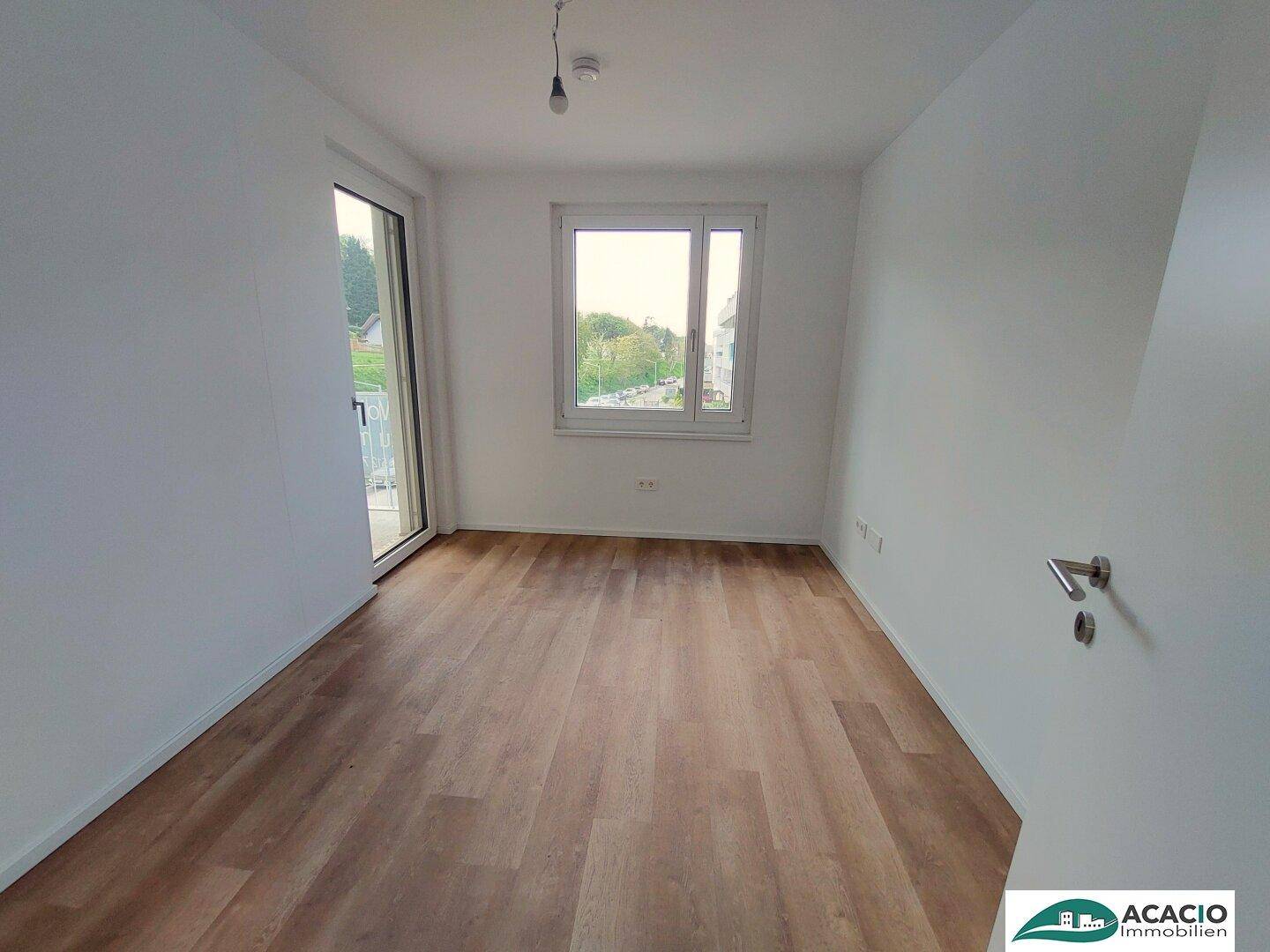 Helles Zimmer mit Holzboden, Fenster und Zugang zu einem Balkon, bietet viel Tageslicht.