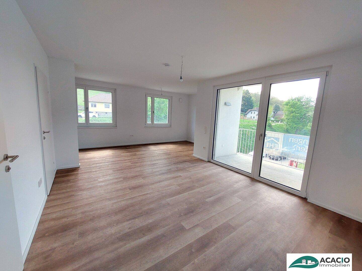 Geräumiges Wohnzimmer mit Holzboden, großen Fenstern und Balkonzugang, bietet einen grünen Ausblick.