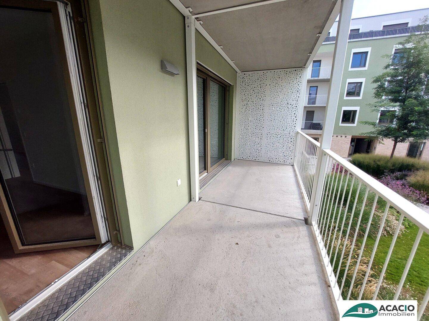 Moderner Balkon mit Betonboden und Blick auf die grüne Umgebung und Nachbargebäude.