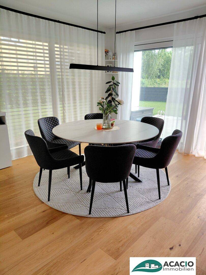 Stilvoller Essbereich mit rundem Tisch, dunklen Stühlen und großen Fenstern für viel Licht.