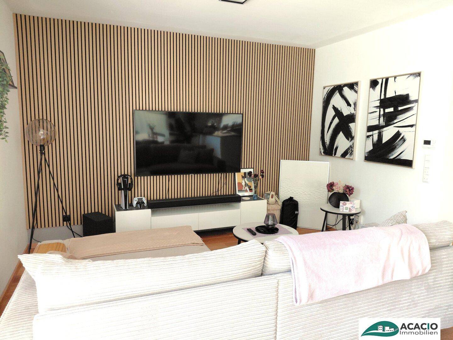 Gemütliches Wohnzimmer mit moderner Holzlamellenwand, großem Fernseher und bequemer Couch.