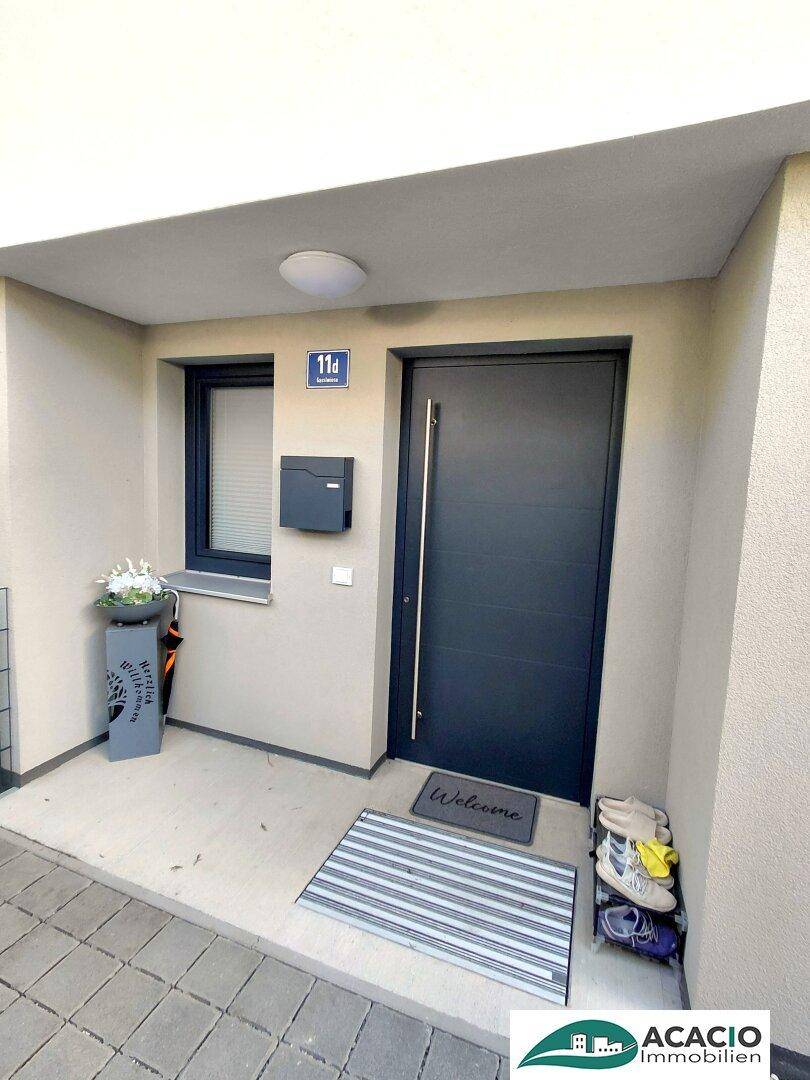 Eingangsbereich eines modernen Hauses mit dunkler Tür und kleiner Fensterfront.