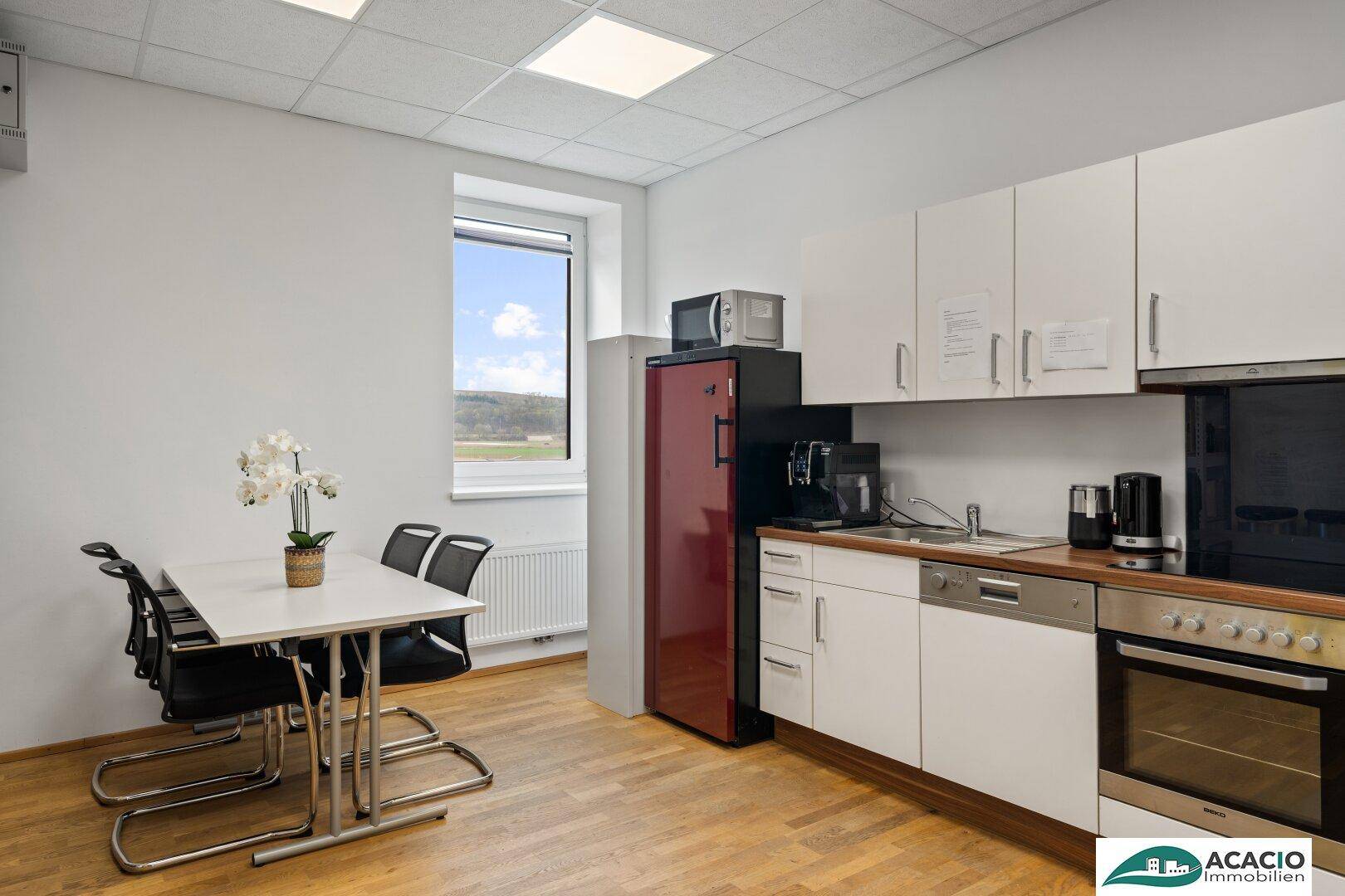 Funktionale Küche mit weißen Schränken, Essbereich und Fenster mit Blick ins Grüne.