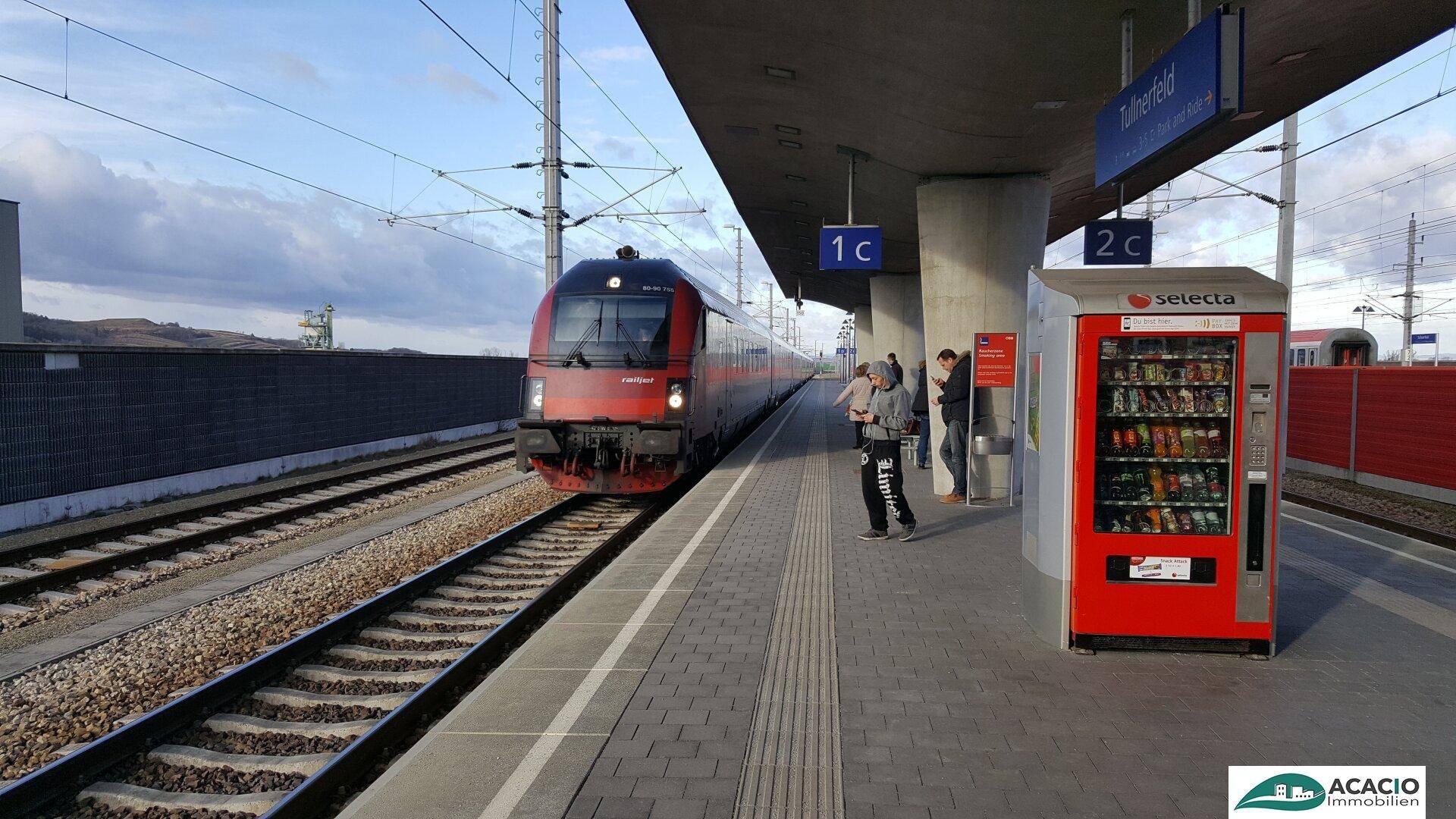 Zug am Bahnsteig eines modernen Bahnhofs mit Fahrgästen und einem Verkaufsautomaten, bereit zur Abfahrt.