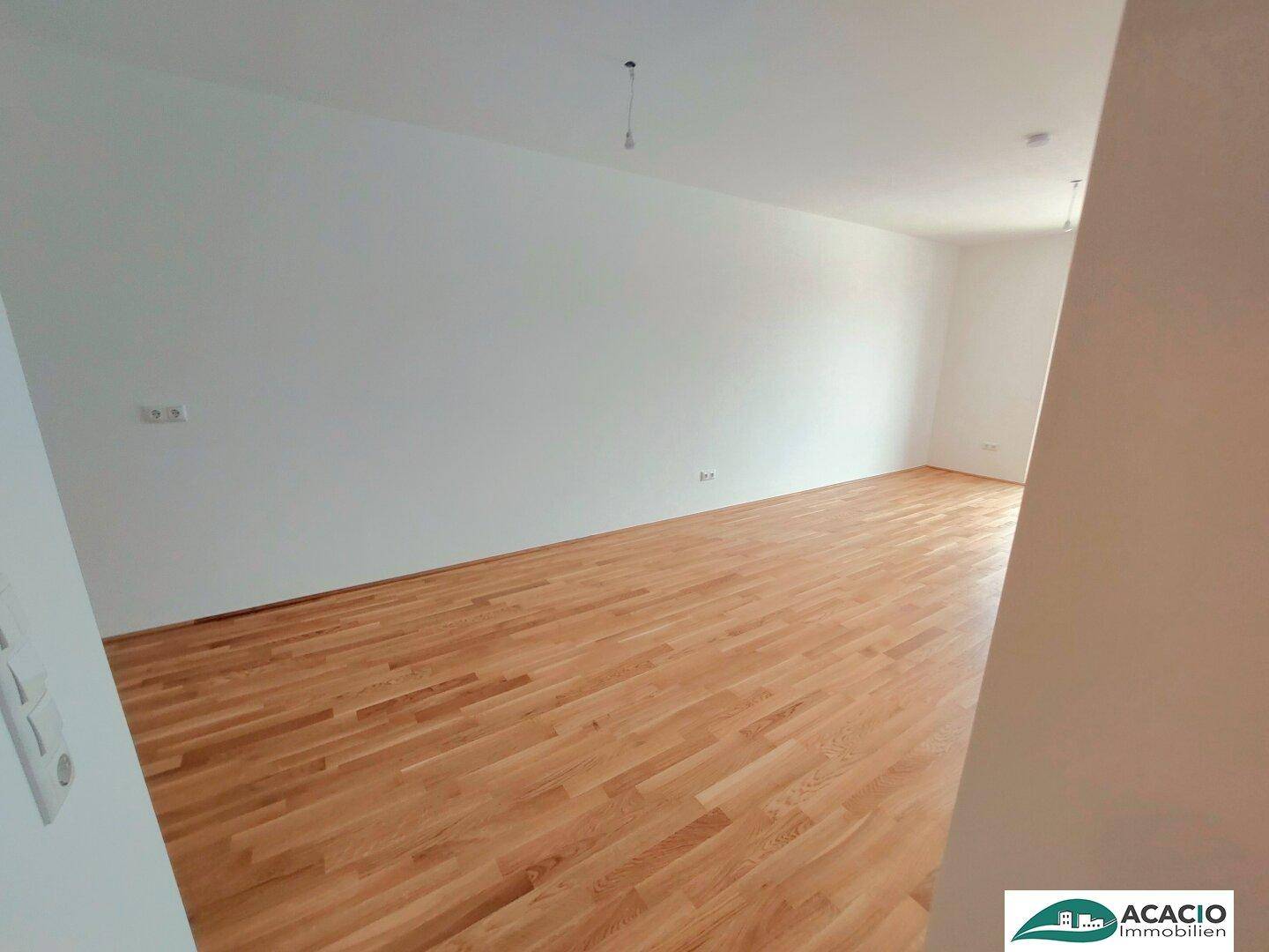 Geräumiges, leeres Zimmer mit hellem Holzboden und weißen Wänden, bereit zur Einrichtung.