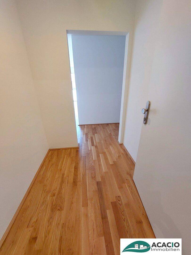 Schmaler Flur mit Holzboden, der den Übergang zu einem weiteren hellen Raum bildet.