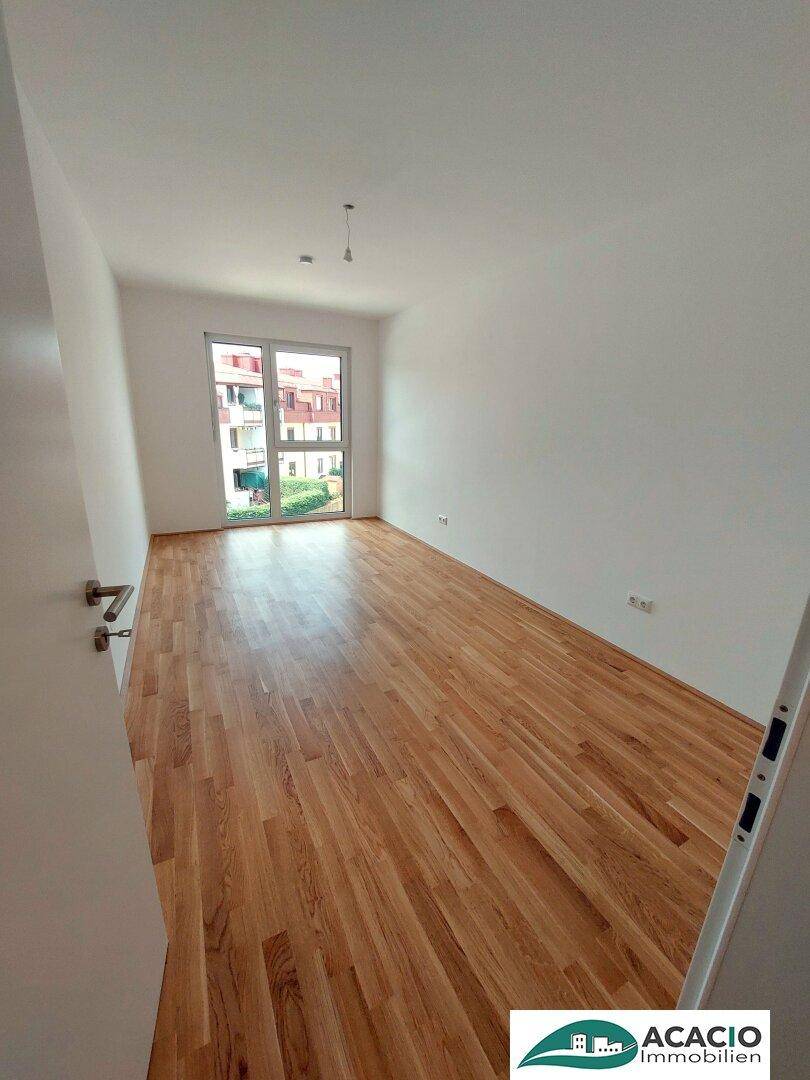 Helles Schlafzimmer mit Holzboden und großem Fenster, das viel Tageslicht hereinlässt.
