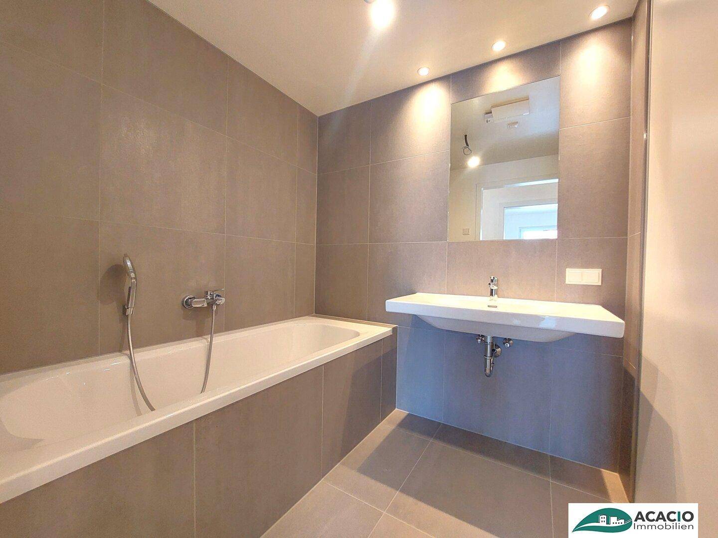 Modernes Badezimmer mit Badewanne, Einzelwaschbecken und eleganten grauen Fliesen.