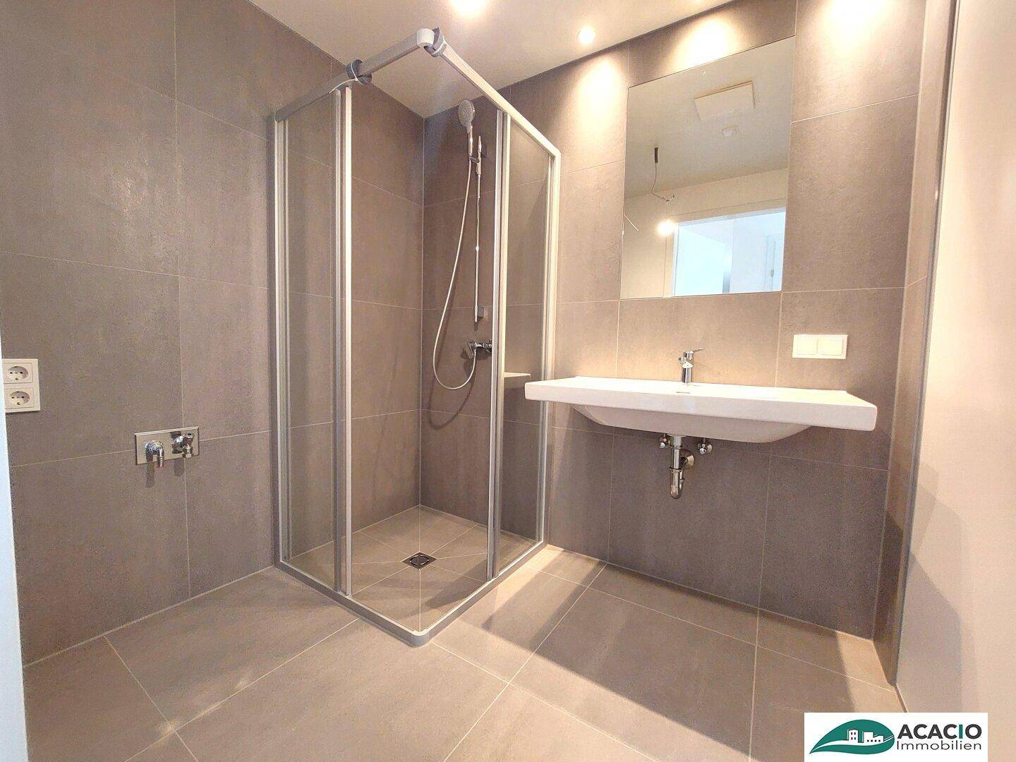Modernes Badezimmer mit grauen Fliesen, einer geräumigen Duschkabine und einem einzelnen Waschbecken.