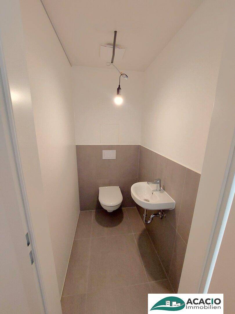 Praktisches Gäste-WC mit modernen Fliesen, wandhängendem WC und kleinem Handwaschbecken.