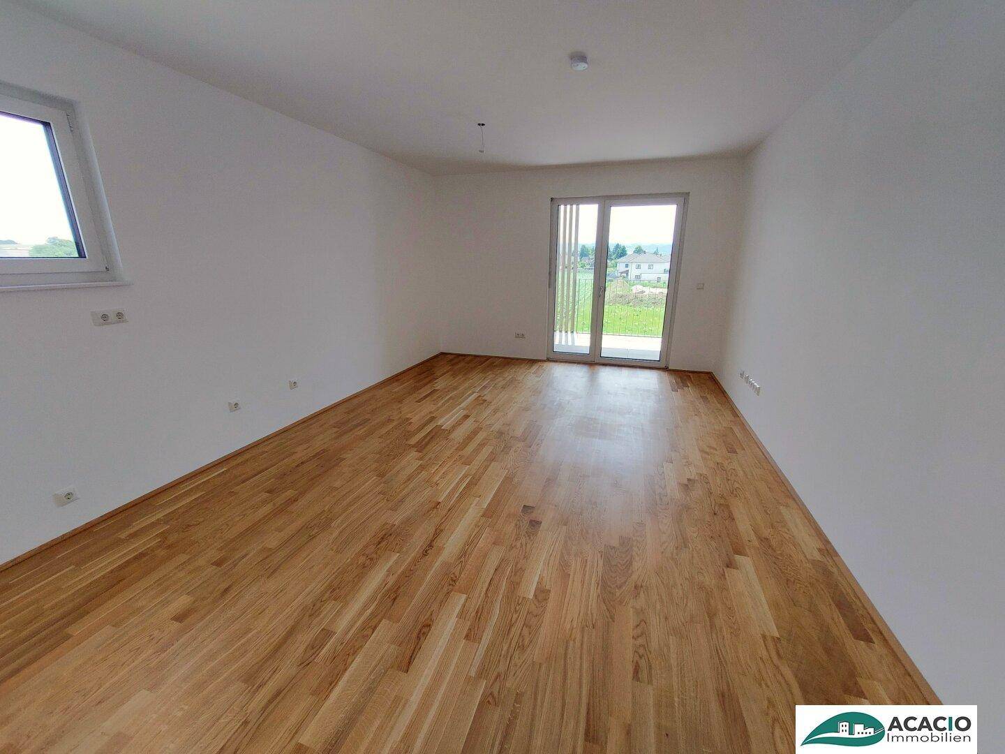 Helles Wohnzimmer mit Parkettboden und Zugang zu einem Balkon oder einer Terrasse mit Blick ins Grüne.