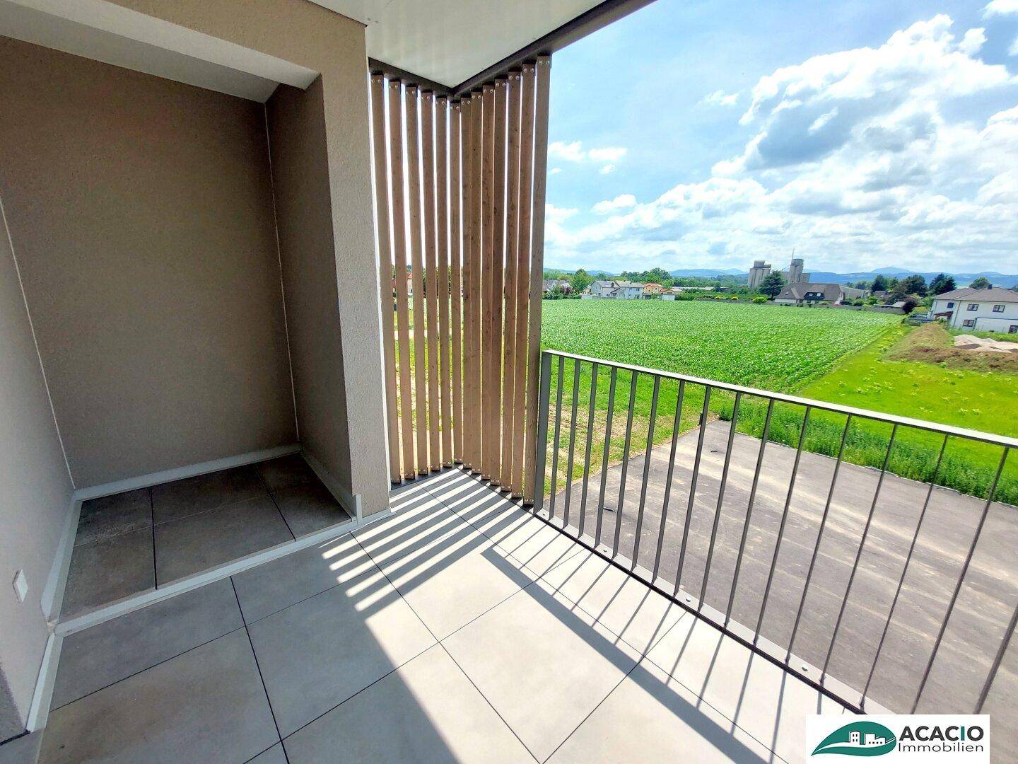 Sonniger Balkon mit Fliesenboden und weitem Blick über grüne Felder und die Landschaft.
