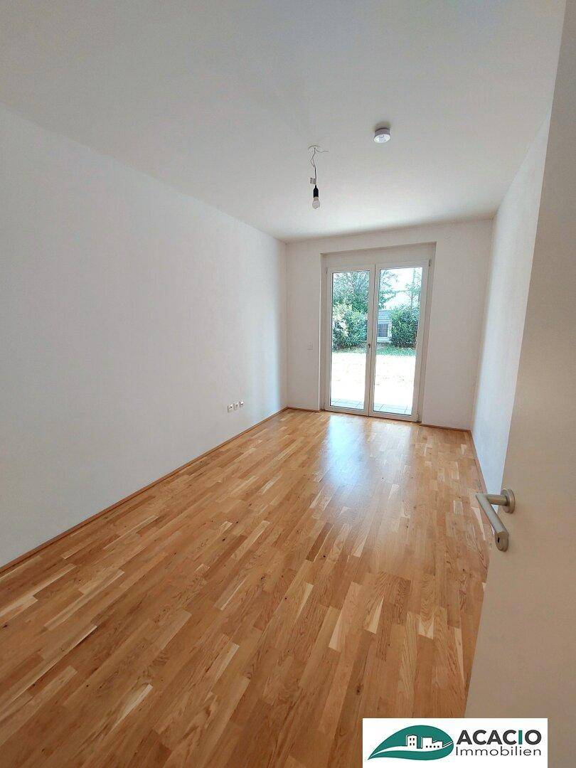 Helles Schlafzimmer mit Parkettboden und Zugang zu einem Außenbereich.