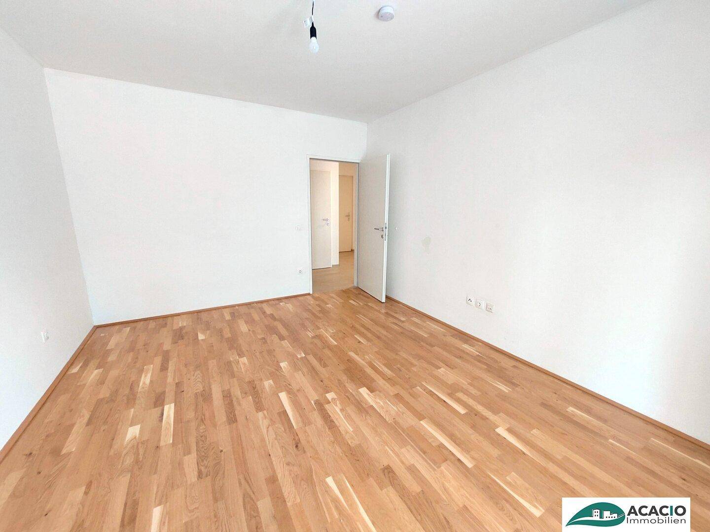 Leeres Zimmer mit Parkettboden und weiß gestrichenen Wänden, ideal als Schlaf- oder Arbeitszimmer.
