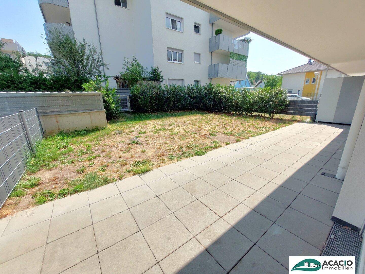 Große gepflasterte Terrasse mit angrenzendem Gartenbereich und Hecke.