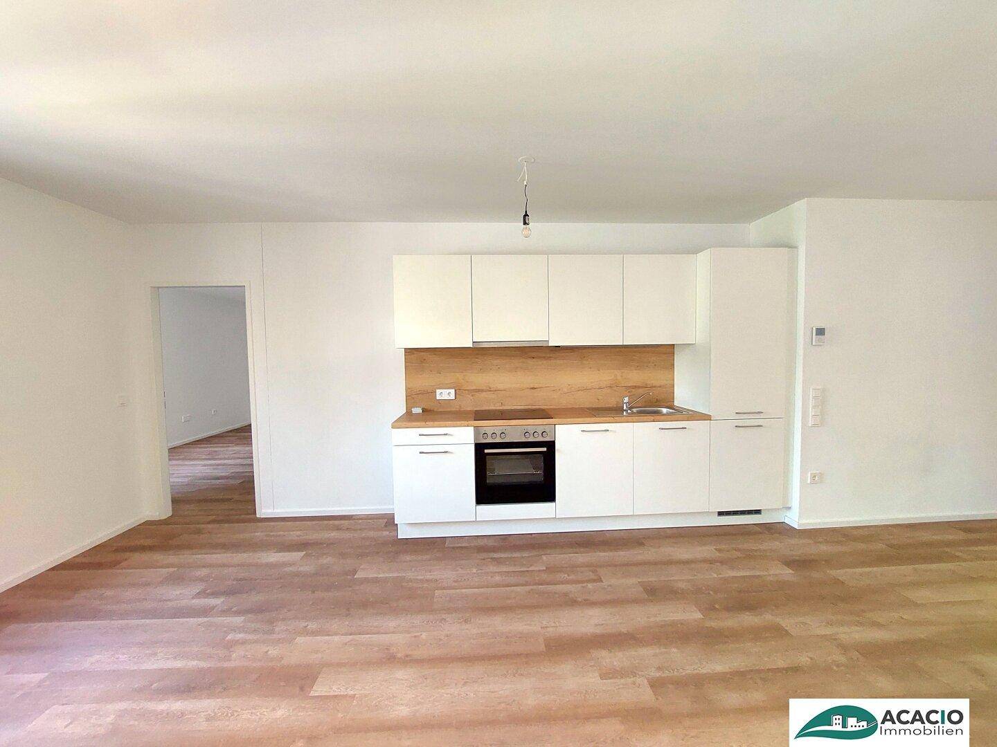 Moderne Küchenzeile mit weißen Schränken, Holzarbeitsplatte und integriertem Backofen in hellem Wohnraum.