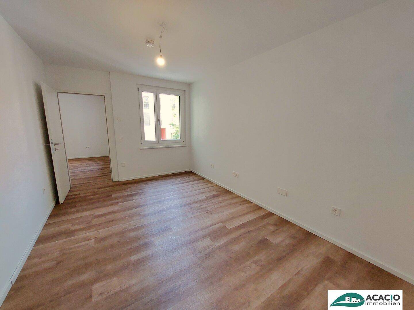 Geräumiges Schlafzimmer mit hellem Laminatboden und großem Fenster, das viel Tageslicht hereinlässt.