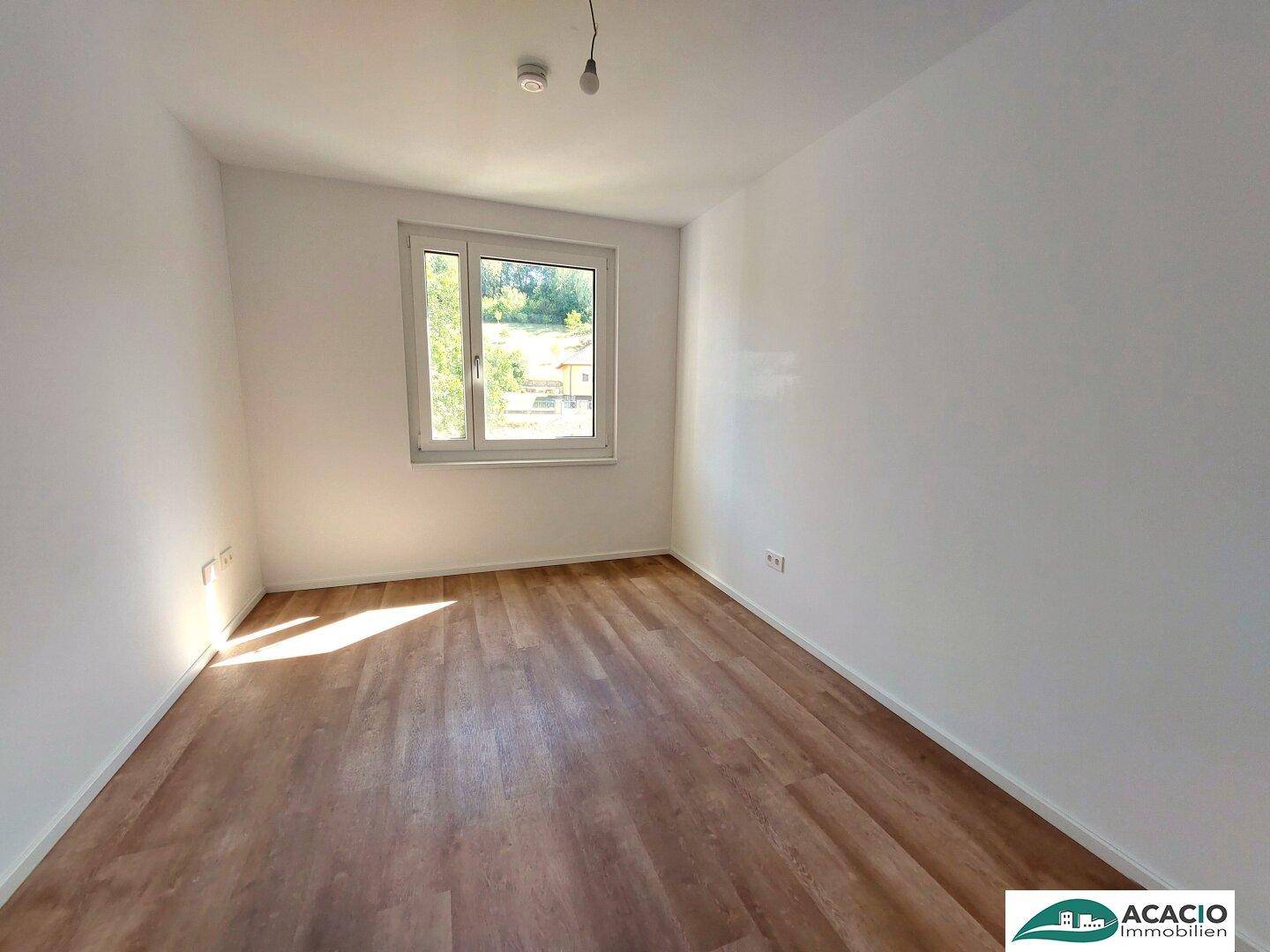 Geräumiges Schlafzimmer mit Laminatboden und Fenster, das viel Tageslicht hereinlässt.