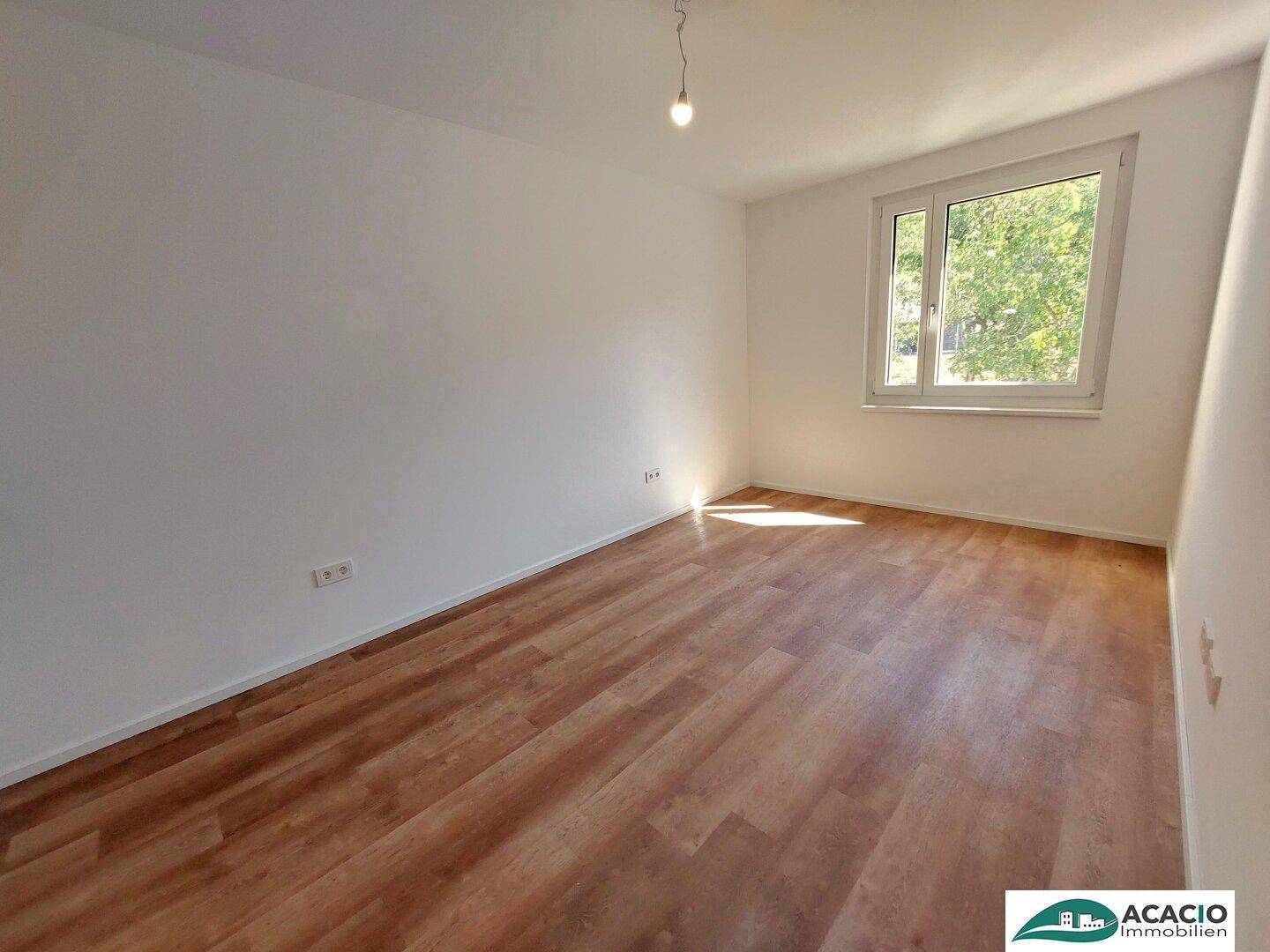 Helles Schlafzimmer mit Laminatboden und großem Fenster mit Blick ins Grüne.