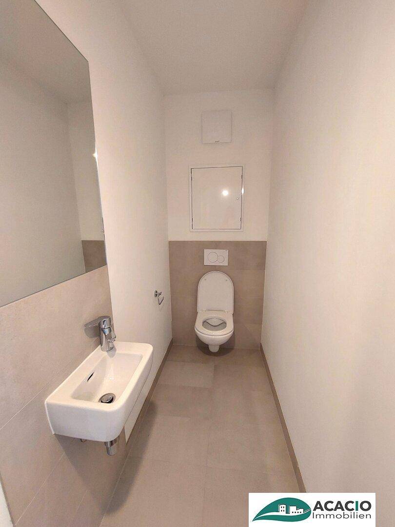 Funktionale Gästetoilette mit wandhängendem WC und kleinem Waschbecken, modern gefliest.