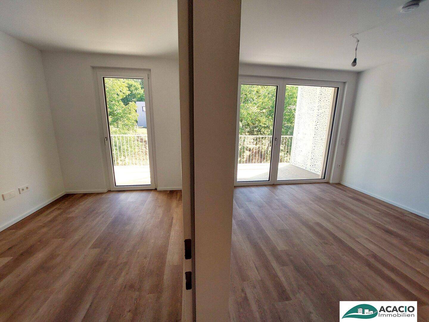 Lichtdurchfluteter Raum mit zwei großen Schiebetüren zum Balkon und modernem Laminatboden.