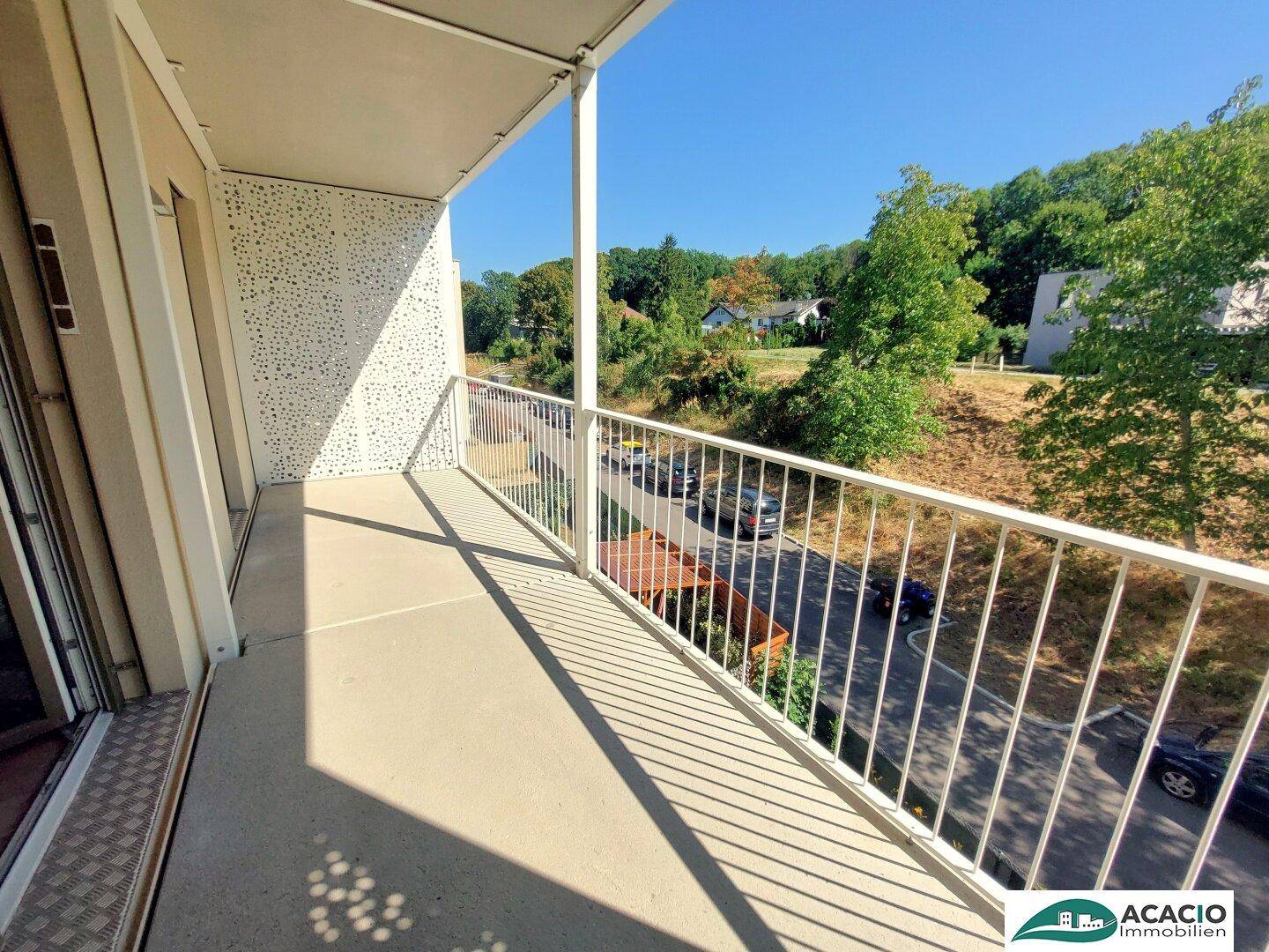 Sonniger Balkon mit weißem Geländer und Blick ins Grüne, ideal zum Entspannen im Freien.
