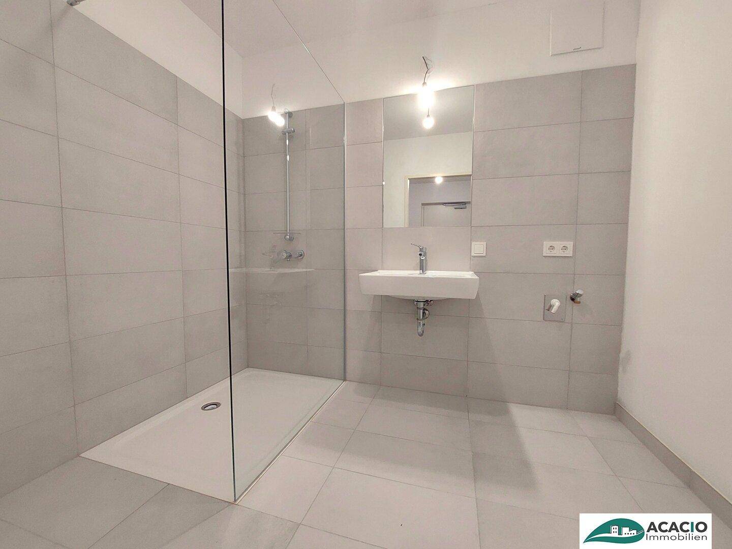 Modernes Badezimmer mit ebenerdiger Dusche, großformatigen Fliesen und Einzelwaschbecken.
