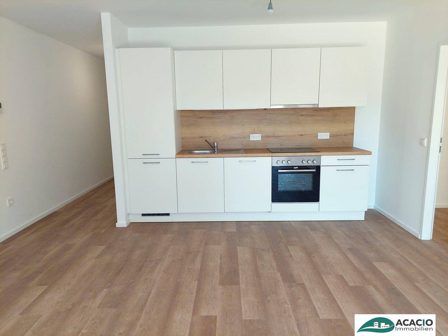 Moderne Einbauküche mit weißen Fronten, Backofen und Holzdekor-Arbeitsplatte.