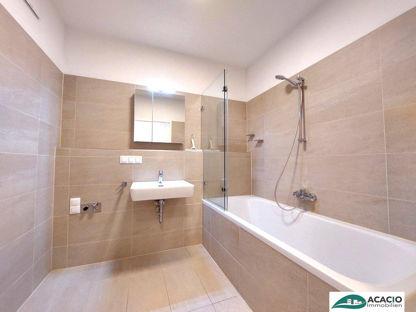 Modernes Badezimmer mit Badewanne, Dusche und beigefarbenen Fliesen, ausgestattet mit einem Spiegelschrank.