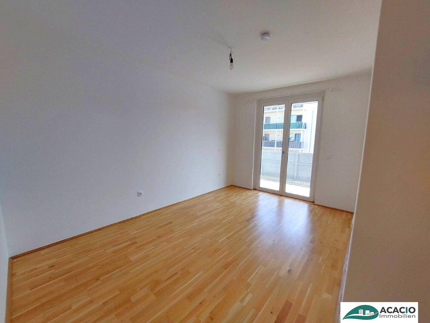 Geräumiges Zimmer mit Parkettboden und großen Fenstern, die viel Tageslicht hereinlassen.