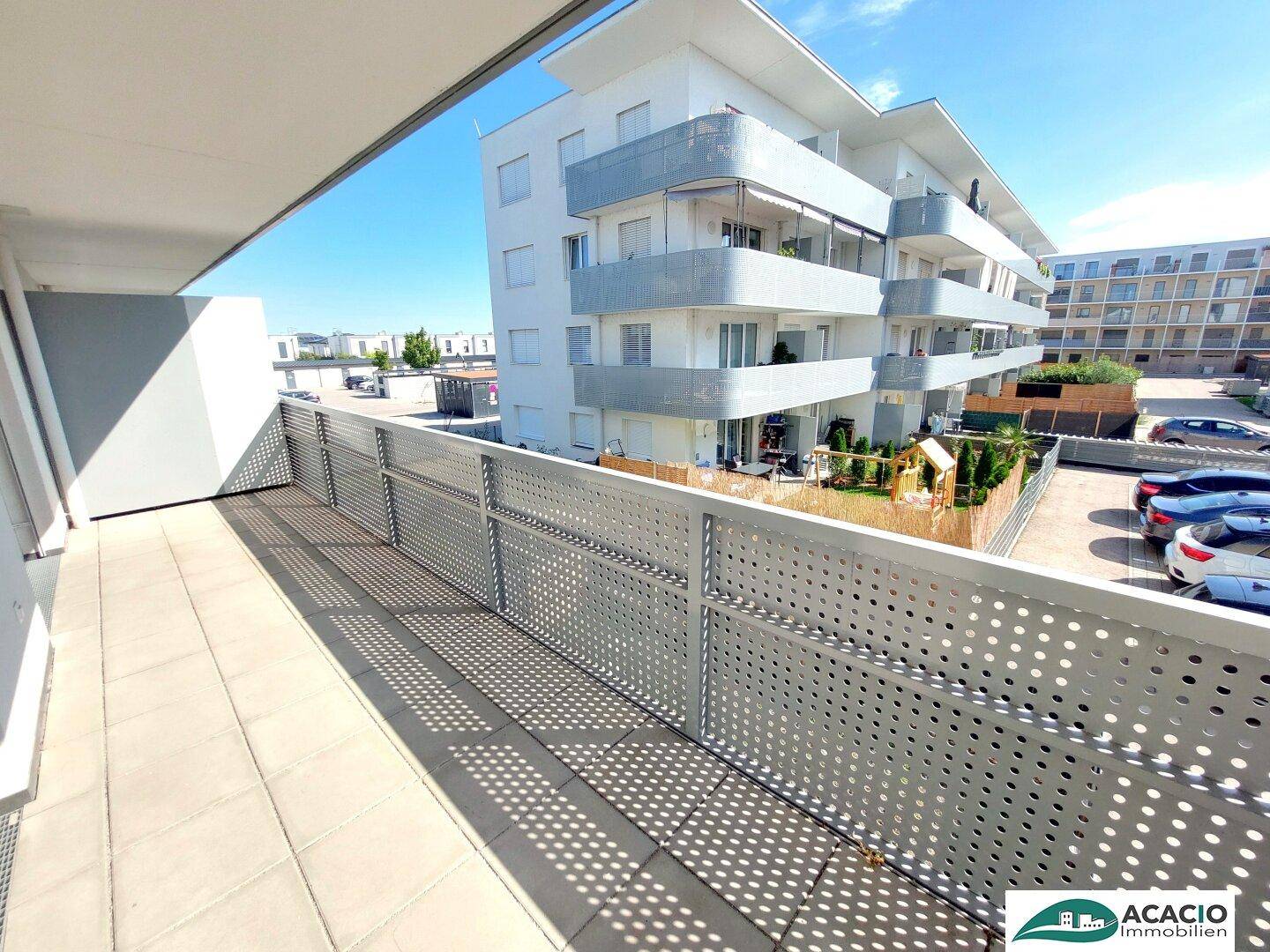 Geräumiger Balkon mit Fliesenboden und Blick auf die moderne Wohnanlage.