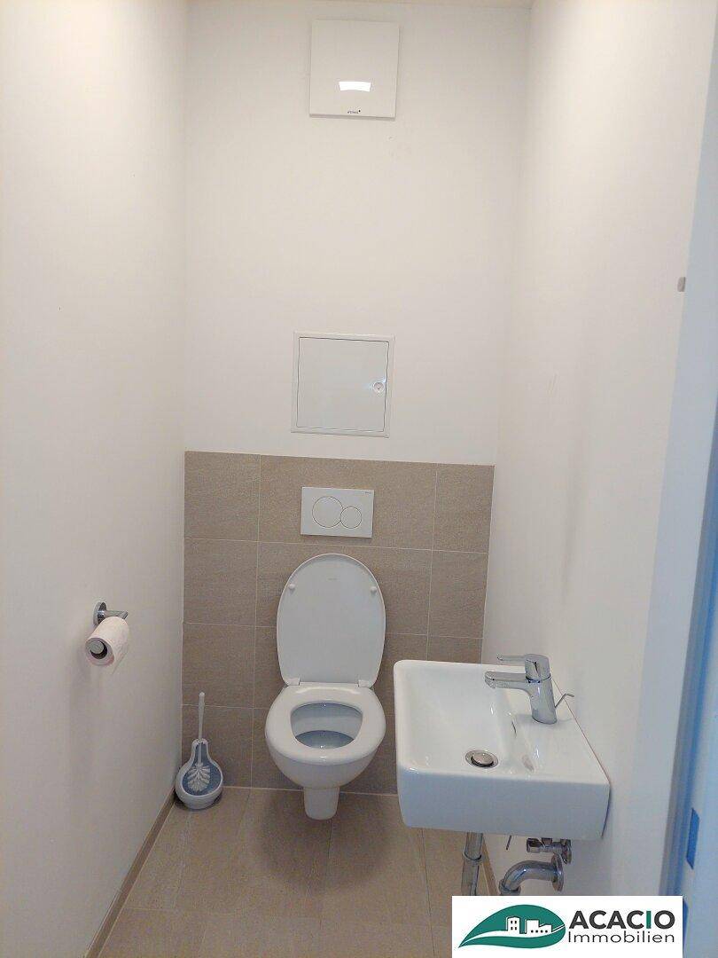 Separates Gäste-WC mit Wand-WC und kleinem Handwaschbecken, hell gefliest.