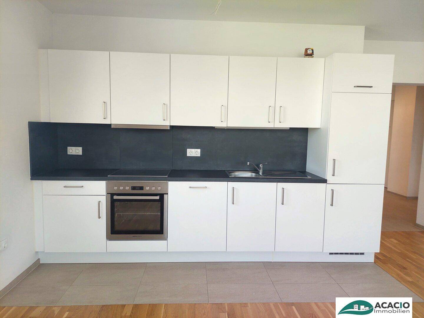 Moderne Einbauküche mit weißen Fronten, schwarzer Arbeitsplatte und integriertem Backofen.